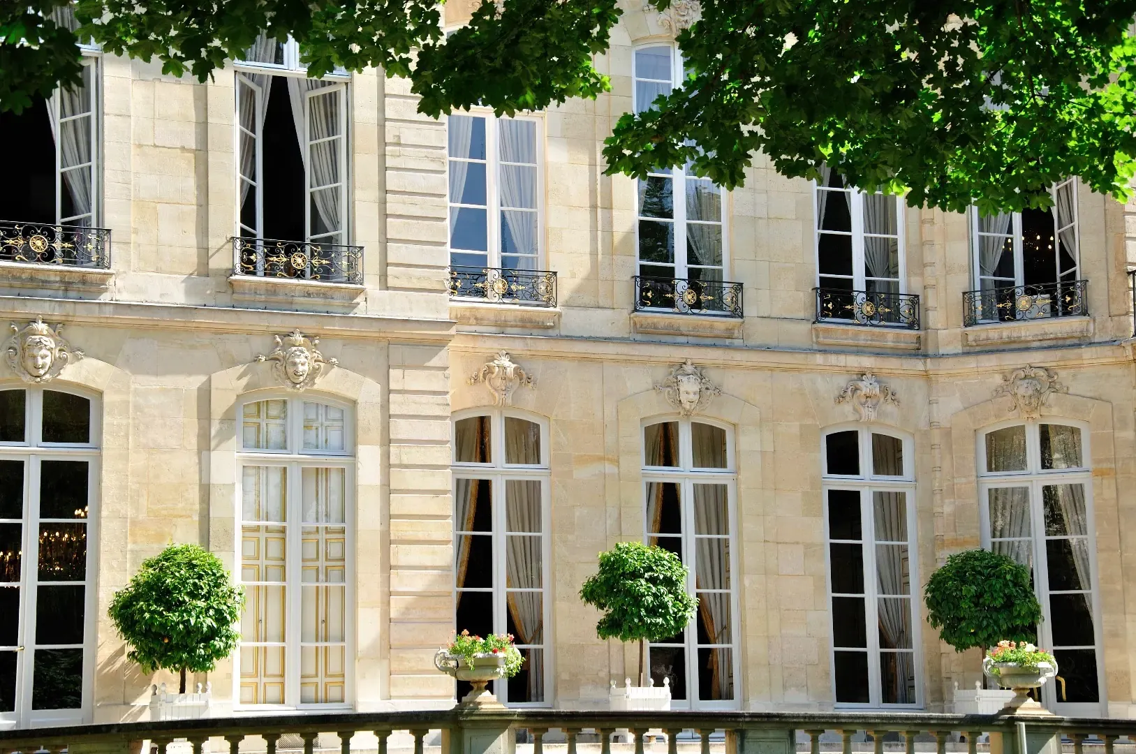 Façade en pierre claire d'une demeure bourgeoise avec balcons en fer forgé et arbres taillés.