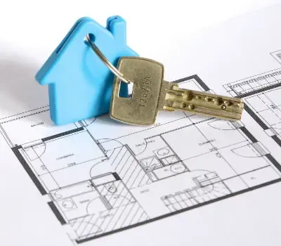 Porte-clés en forme de maison et cadenas posés sur un plan immobilier.